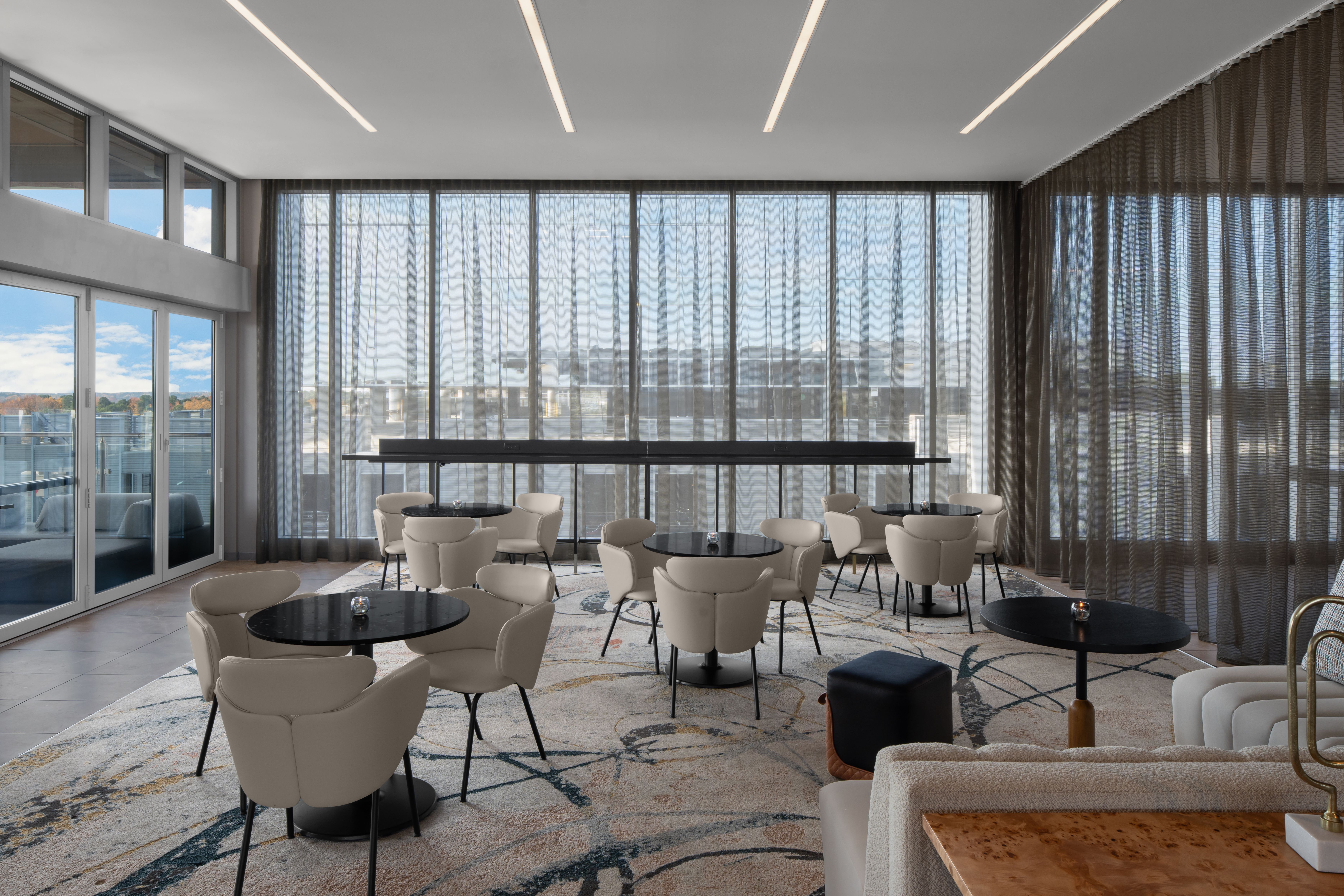 A sophisticated lounge space at AC Hotels Raleigh, featuring floor-to-ceiling windows, elegant seating, and a relaxed atmosphere for guests.